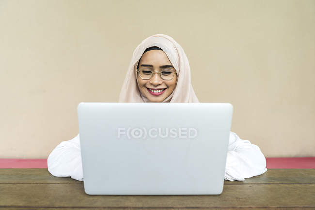 Молодая азиатская мусульманка использует ноутбук в помещении — стоковое фото