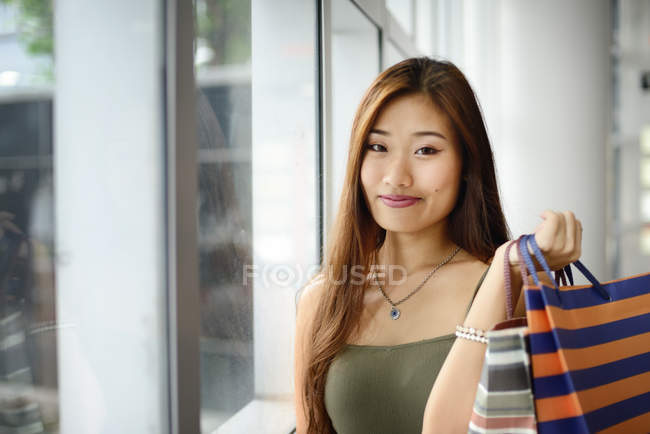 Giovane donna asiatica in shopping mall holding bag — Foto stock