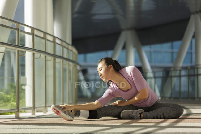 A young asian woman is stretching before her daily running workout in Singapores city. — Stock Photo