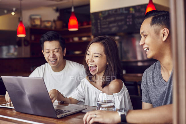Young asian friends using laptop together in bar — Stock Photo