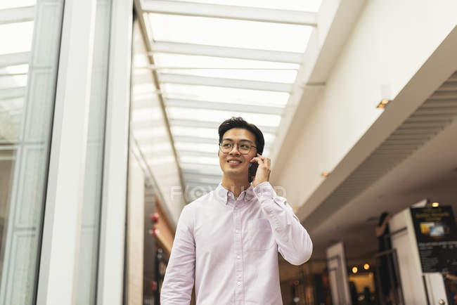 Молодой случайный азиатский мужчина, использующий телефон в торговом центре — стоковое фото
