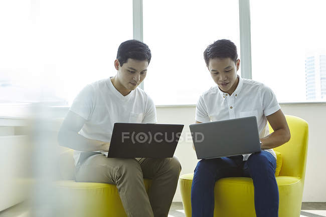 Молодые азиатские бизнесмены, работающие с ноутбуками в современном офисе — стоковое фото