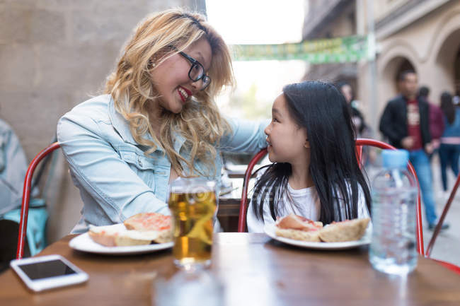 Retrato de jovem mãe feliz com sua filha comendo em um café — Fotografia de Stock
