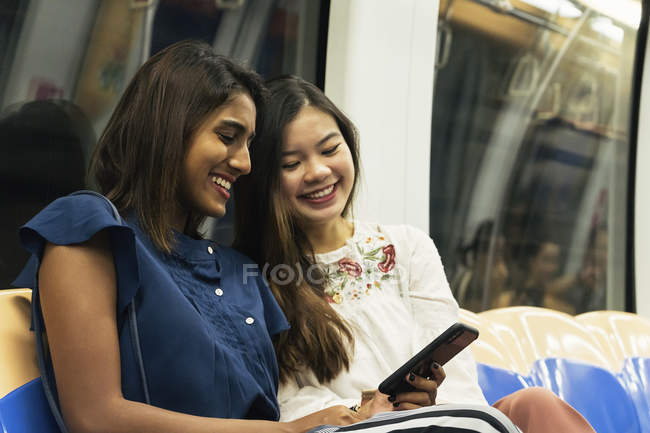 Jovem casual asiático meninas compartilhamento smartphone no trem — Fotografia de Stock
