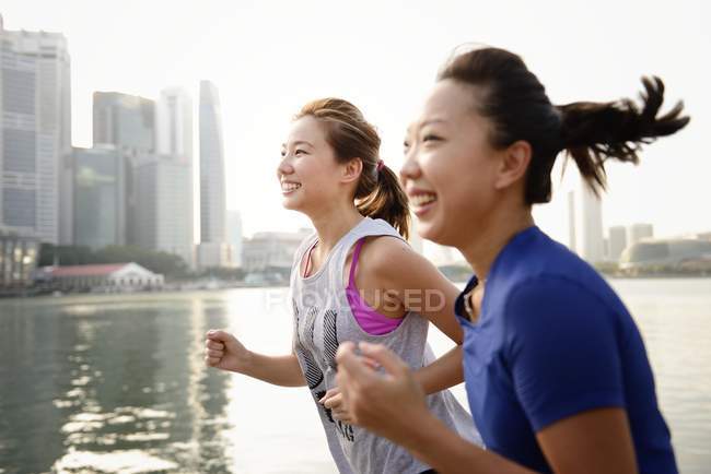 Dos mujeres deportivas corriendo al aire libre contra el agua - foto de stock