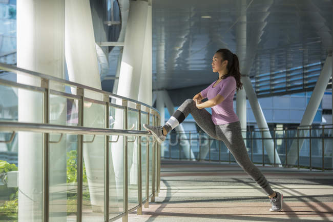 A young asian woman is stretching before her daily running workout in Singapores city. — Stock Photo