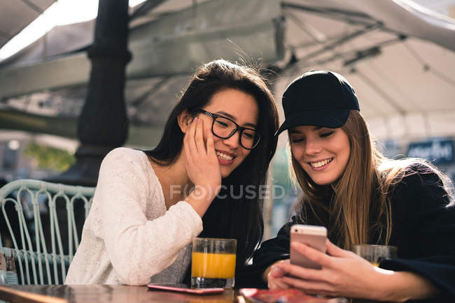 Китайские и европейские симпатичные молодые женщины смотрят на смартфон на террасе Мадрида — стоковое фото