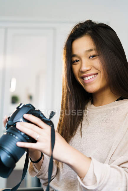 Joven mujer china mirando a la cámara sonriendo y sosteniendo una cámara - foto de stock
