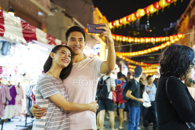 Young asian couple spending time together on traditional bazaar at Chinese New Year and taking selfie — Stock Photo