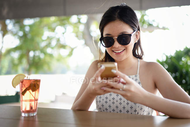 Jovem atraente asiático mulher em óculos de sol usando smartphone — Fotografia de Stock