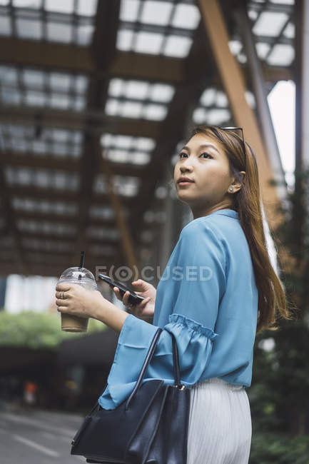 Attractive young asian girl using smartphone and coffee cup — Stock Photo
