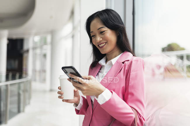 Молодая привлекательная азиатка, использующая смартфон в торговом центре — стоковое фото