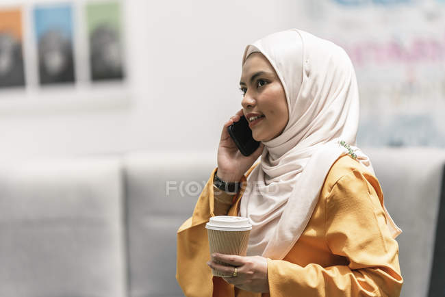 Junge asiatische Geschäftsfrau im Hijab mit Smartphone im modernen Büro — Stockfoto
