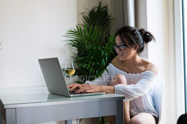 Chinesische hübsche Frau arbeitet drinnen mit ihrem Laptop und einem Glas Wein — Stockfoto