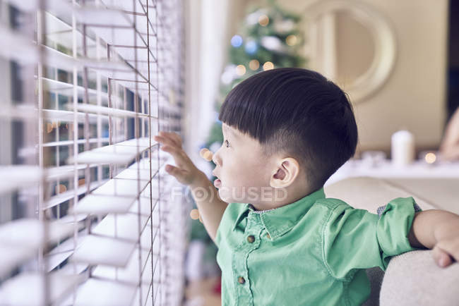 Pequeño asiático chico buscando fuera de ventana en Navidad - foto de stock