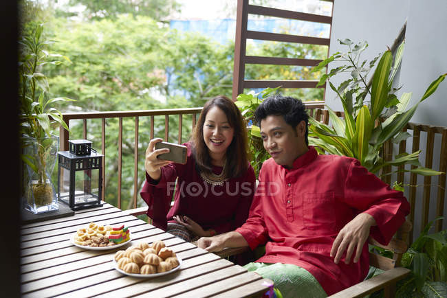 Joven asiático pareja celebrando hari raya en Singapur y tomando selfie - foto de stock
