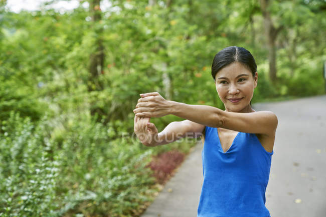 Mujer de mediana edad calentándose en los jardines botánicos antes de correr - foto de stock