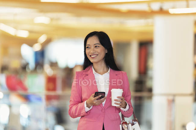 Молода приваблива азіатська жінка використовує смартфон у торговому центрі — стокове фото
