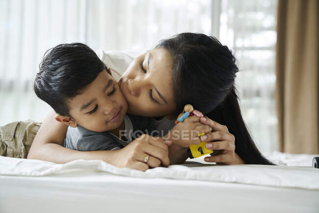 Mère collant avec son fils sur le lit — Photo de stock