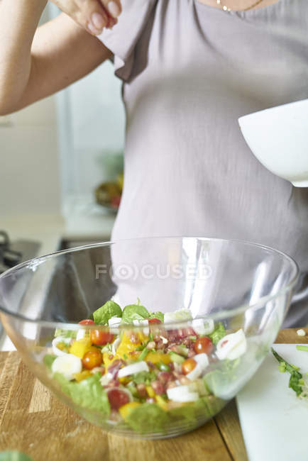 Imagen recortada de la mujer ensalada de cocina en la cocina - foto de stock