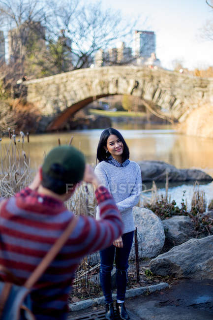 Young man photographing asian girl against lake — Stock Photo