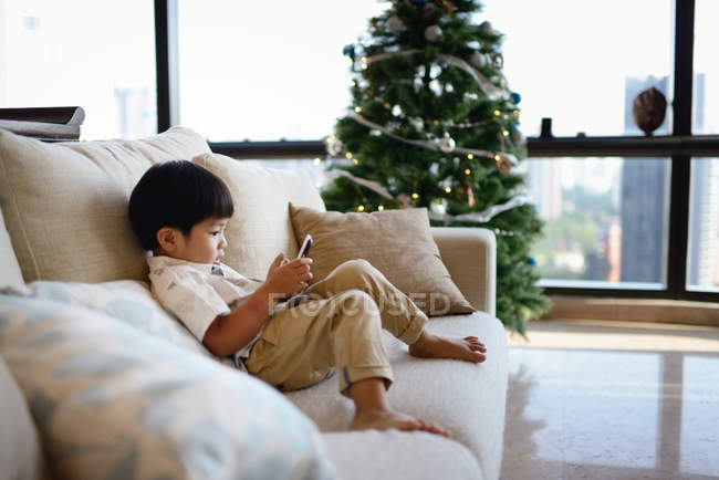 Asiático família celebrando Natal feriado, menino sentado no sofá com celular — Fotografia de Stock
