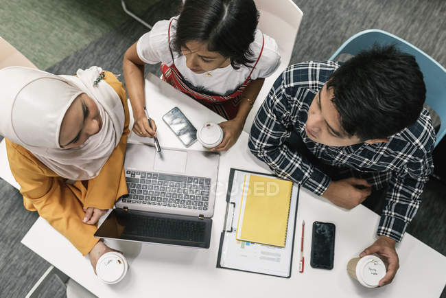 Вид зверху молодих мультикультурних бізнесменів, що працюють з ноутбуком в сучасному офісі — стокове фото