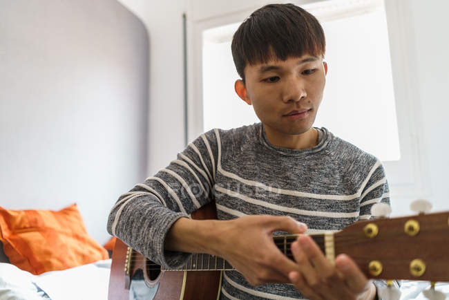 Young asian man playing guitar at home — Stock Photo