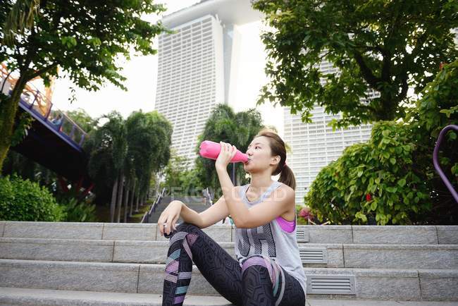Молода азіатська спортивна жінка п'є воду з пляшки — стокове фото