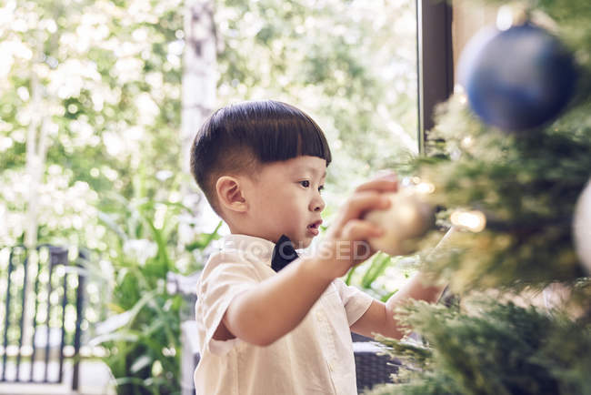 Little asian boy decorating christmas fir tree — Stock Photo