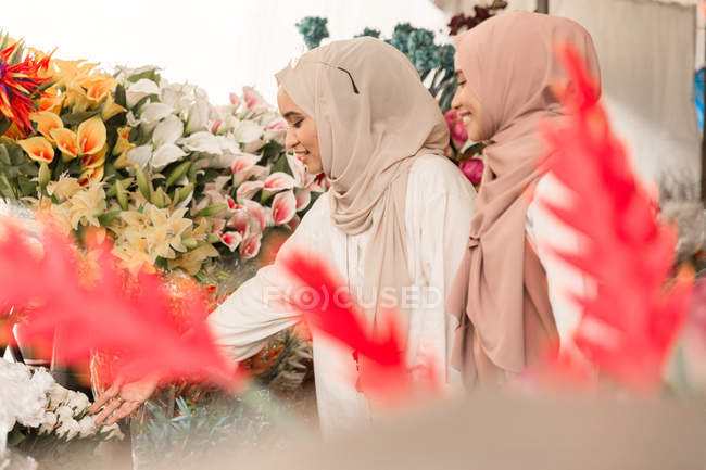 Две юные мусульманки в цветочном магазине весело беседуют — стоковое фото