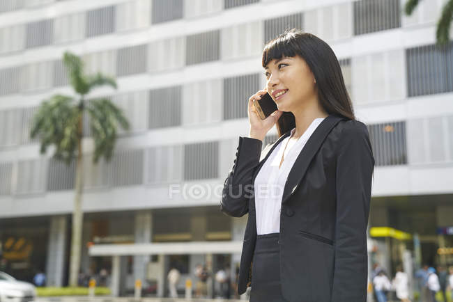 Asian business woman using smartphone on city street — Stock Photo