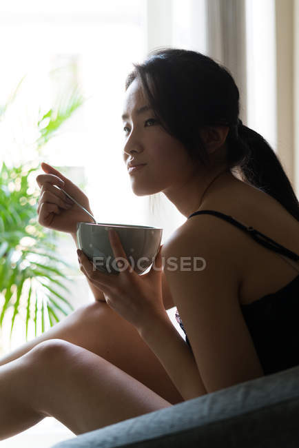 Китайская молодая женщина завтракает на диване дома — стоковое фото