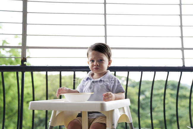 Baby boy eating in a baby seat on the balcony — Stock Photo
