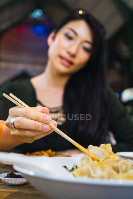 Jeune asiatique femme manger nourriture avec baguettes — Photo de stock