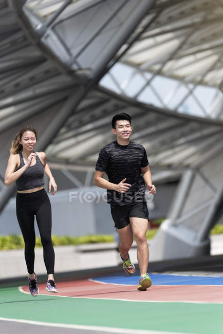 Happy asian sporty couple running on stadium together — Stock Photo