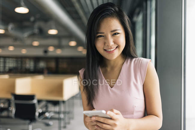 Jeune asiatique succès femme d'affaires avec smartphone dans le bureau moderne — Photo de stock