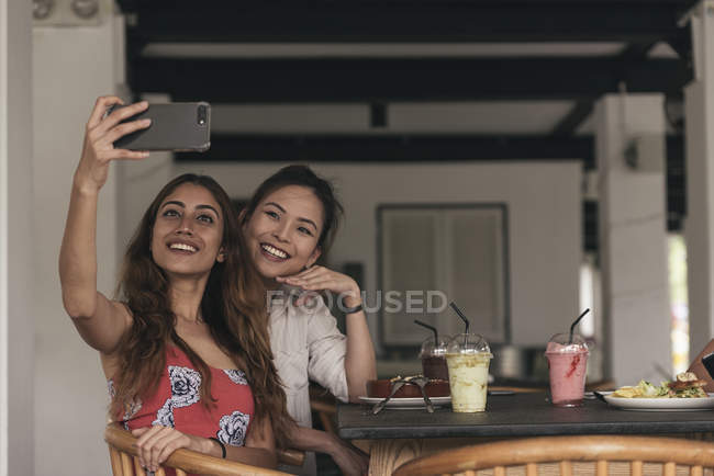 Two young beautiful asian women taking selfie in cafe — Stock Photo