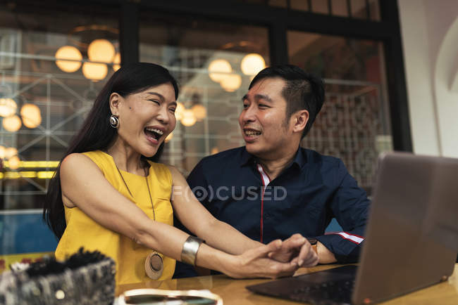 Feliz jovem asiático casal usando laptop e rindo no café — Fotografia de Stock