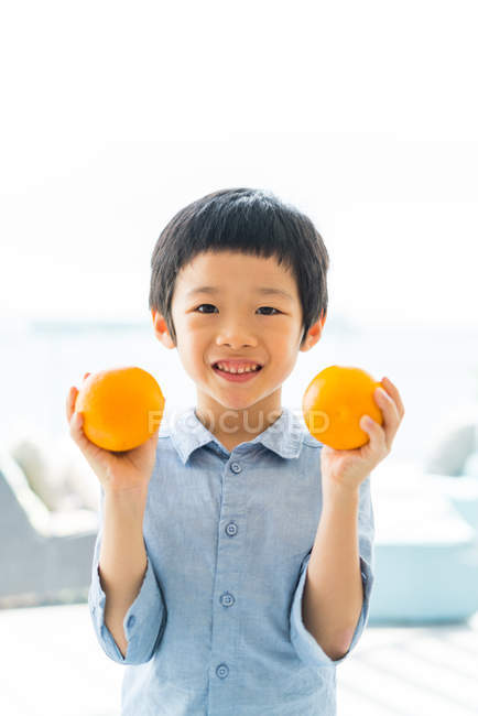 Lindo poco asiático chico holding naranja frutas - foto de stock