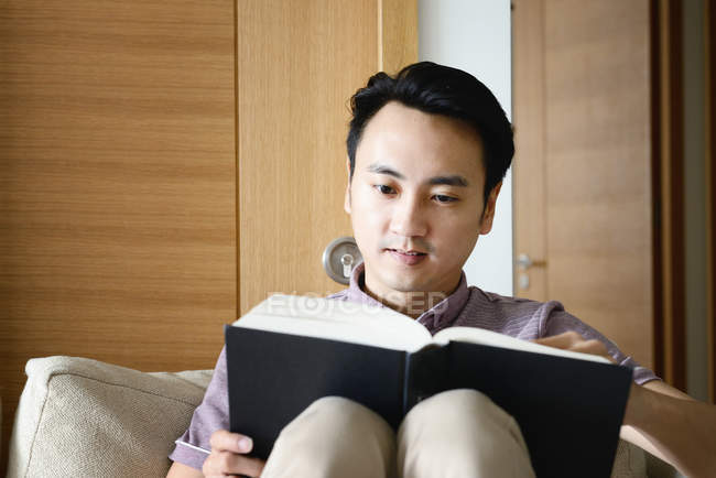 Зрелый азиатский случайный человек, читающий книгу дома — стоковое фото
