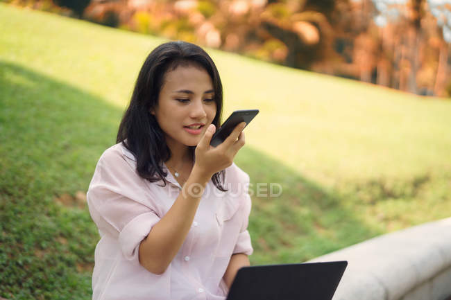Молодая азиатка, использующая смартфон в парке — стоковое фото