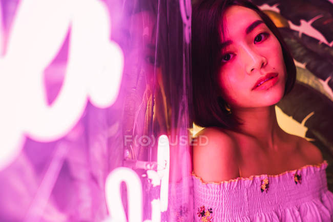 Jovem asiático mulher posando ao lado neon no confortável bar — Fotografia de Stock