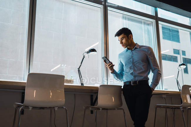 Hombre de negocios adulto joven utilizando el teléfono inteligente en la oficina moderna - foto de stock