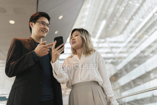 Молодая азиатская пара бизнесменов со смартфоном в аэропорту — стоковое фото