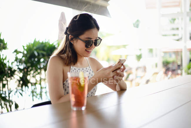 Jeune attrayant asiatique femme en lunettes de soleil en utilisant smartphone — Photo de stock