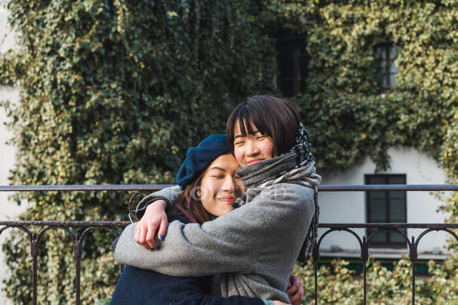 Young adult asian female friends hugging outdoors — Stock Photo