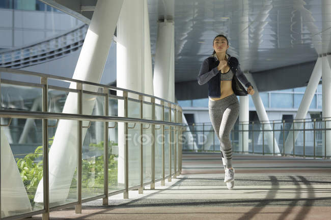 Uma jovem mulher asiática está correndo pela cidade de Singapura no início da manhã. Ela passa por uma seção de arquitetura de aço e vidro . — Fotografia de Stock