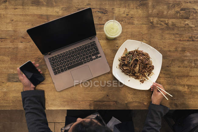 Jovem empresário bem sucedido usando dispositivos eletrônicos e comer macarrão — Fotografia de Stock