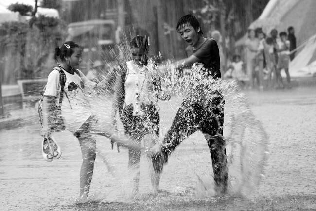 Ho Chi Minh City tem duas estações distintas, que é chuvosa e seca. A estação chuvosa, com uma precipitação média de cerca de 1800mm anualmente (cerca de 150 dias chuvosos por ano), geralmente começa em maio e termina no final de novembro. Durante este período, embora chova intensamente quase todas as tardes, a chuva é curta e clara rapidamente. Jogar à chuva é divertido para os alunos. Eles eram felizes e despreocupados, aparentemente sem preocupações em suas vidas.. — Fotografia de Stock